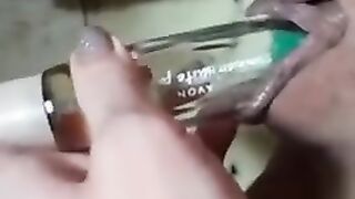 Mädchen schiebt eine Flasche Parfüm in ihre rasierte Muschi und fingert sie